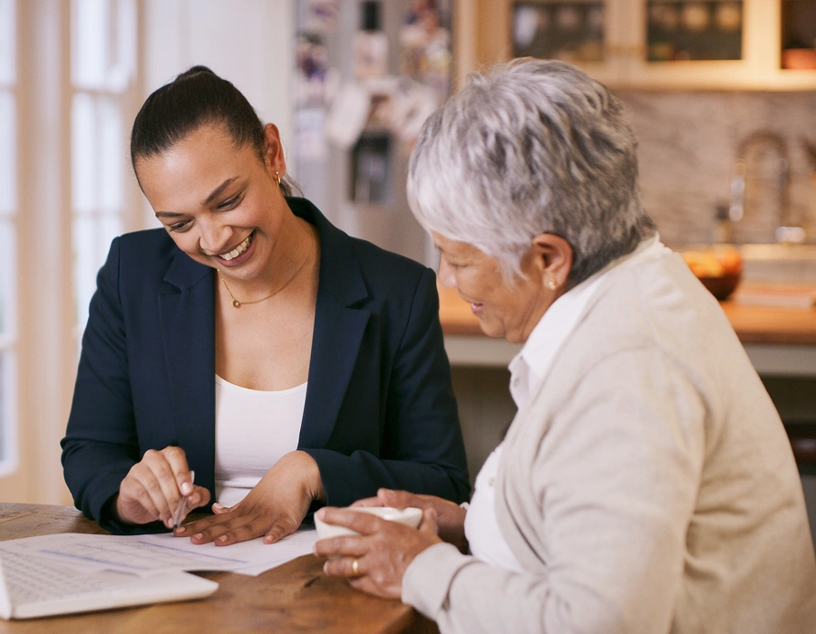 Woman assisting senior with paperwork at table.
