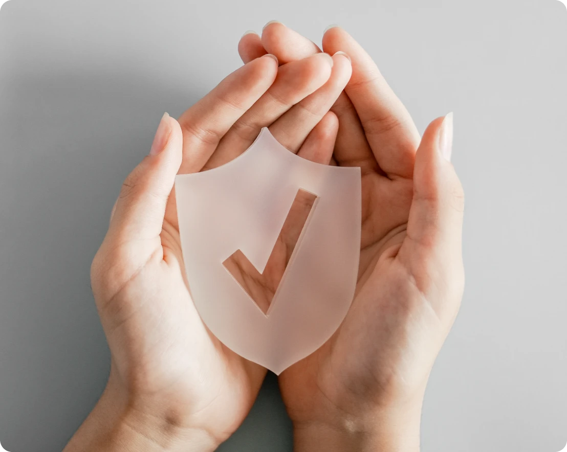 Hands holding shield with check mark.