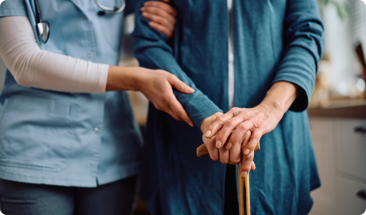 Healthcare worker assisting elderly person with cane.