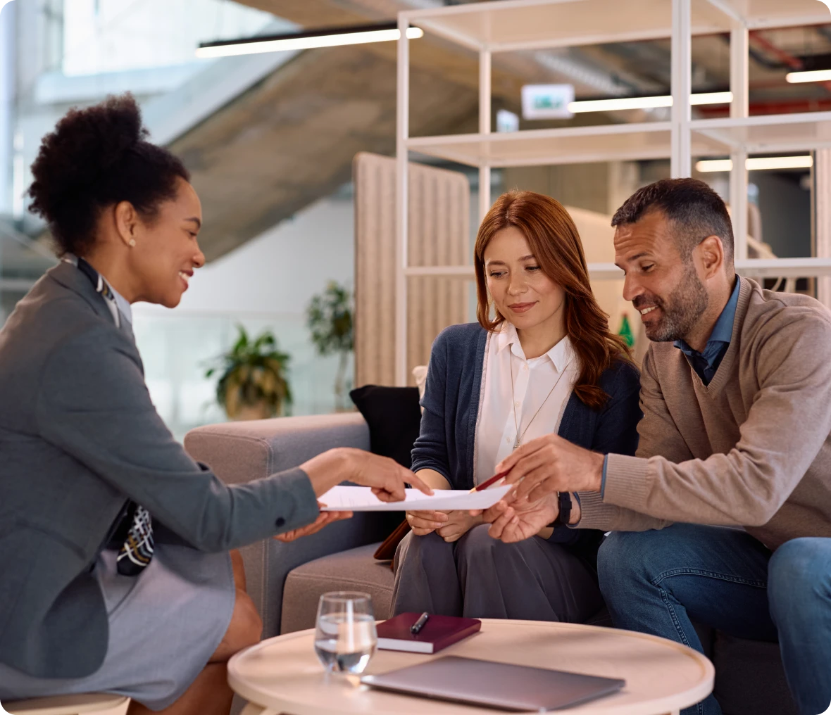 Three people discussing documents in office setting.