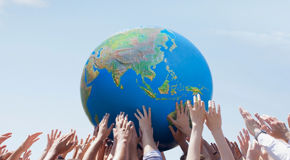 Hands raising a globe under blue sky.